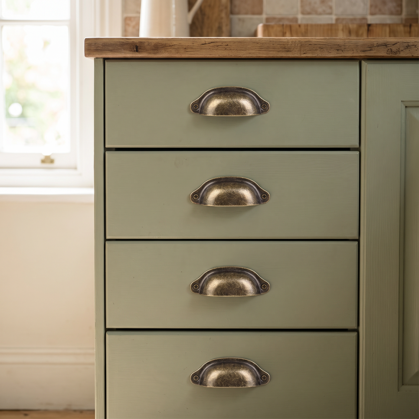 Antique cup pull handles mounted on sage-green farmhouse kitchen drawers